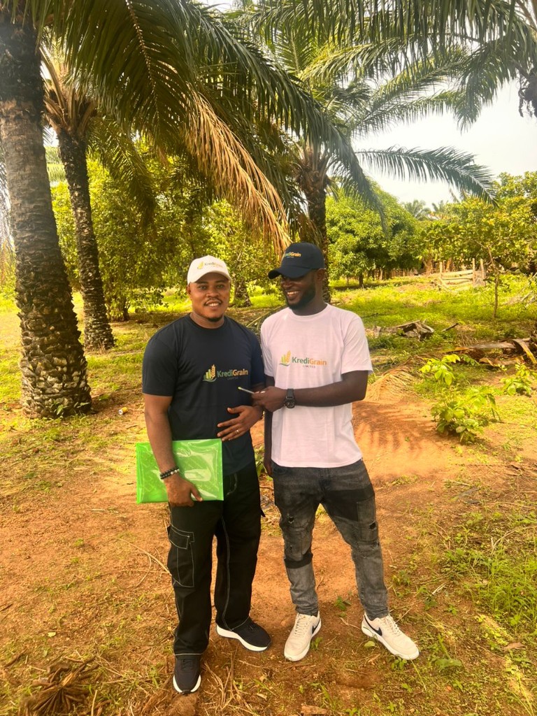 Two KrediGrain team members smiling together in branded apparel in a palm grove