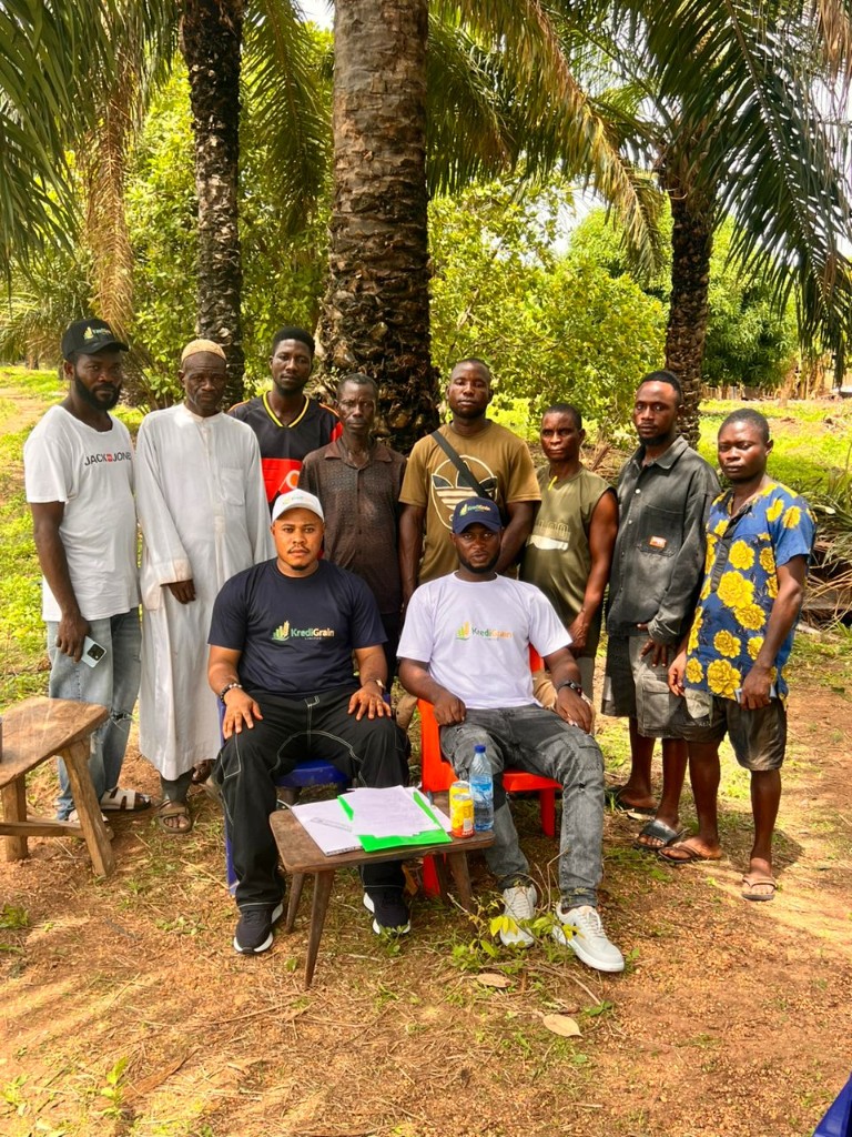Group portrait of men including KrediGrain representatives and local farmers under palm trees