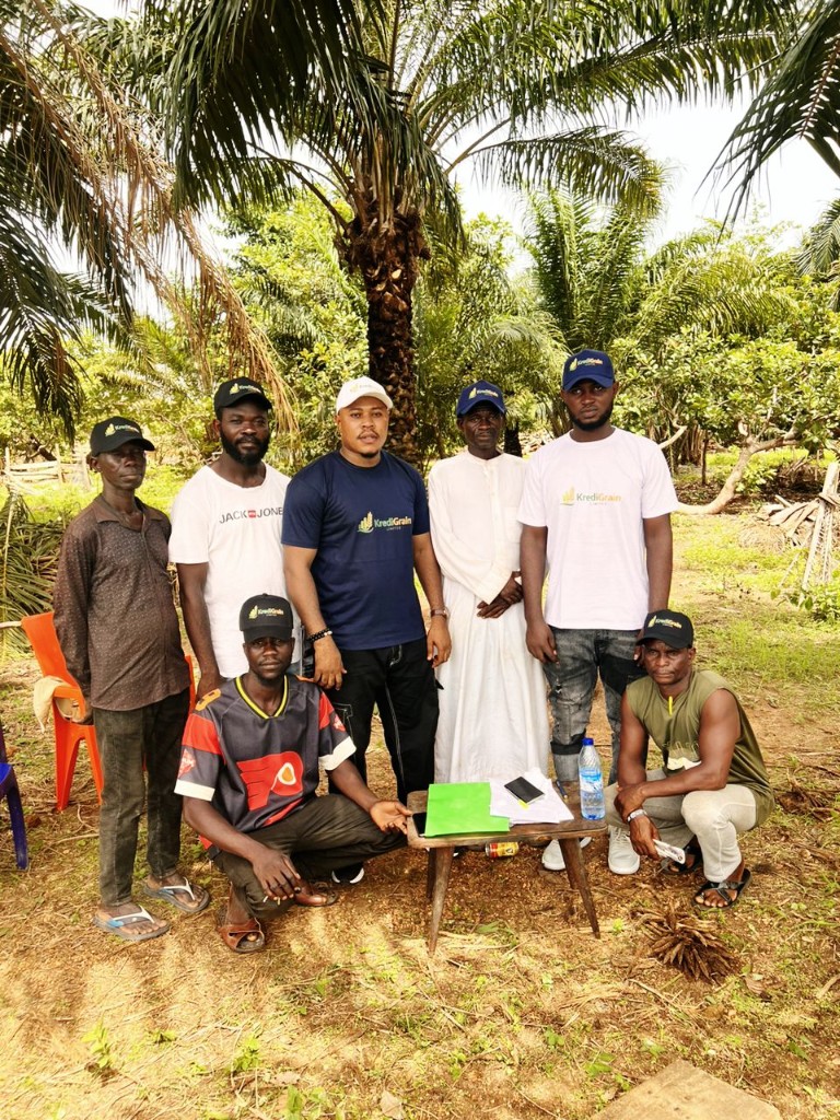 Group of seven men posing outdoors with documents on a small table in a rural setting